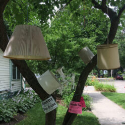 lamps shades hanging from a tree with a sign that says Shade Tree